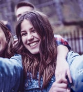 Foto ilustrativa de uma adolescente tirando foto com seus amigos ao fundo