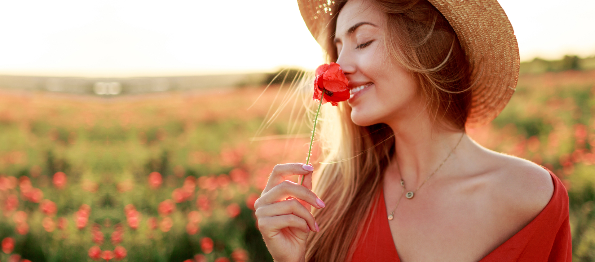 Foto ilustrativa de uma moça feliz cheirando uma flor no campo